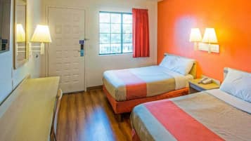 A hotel room with two beds, a window with curtains, a door, and a desk.