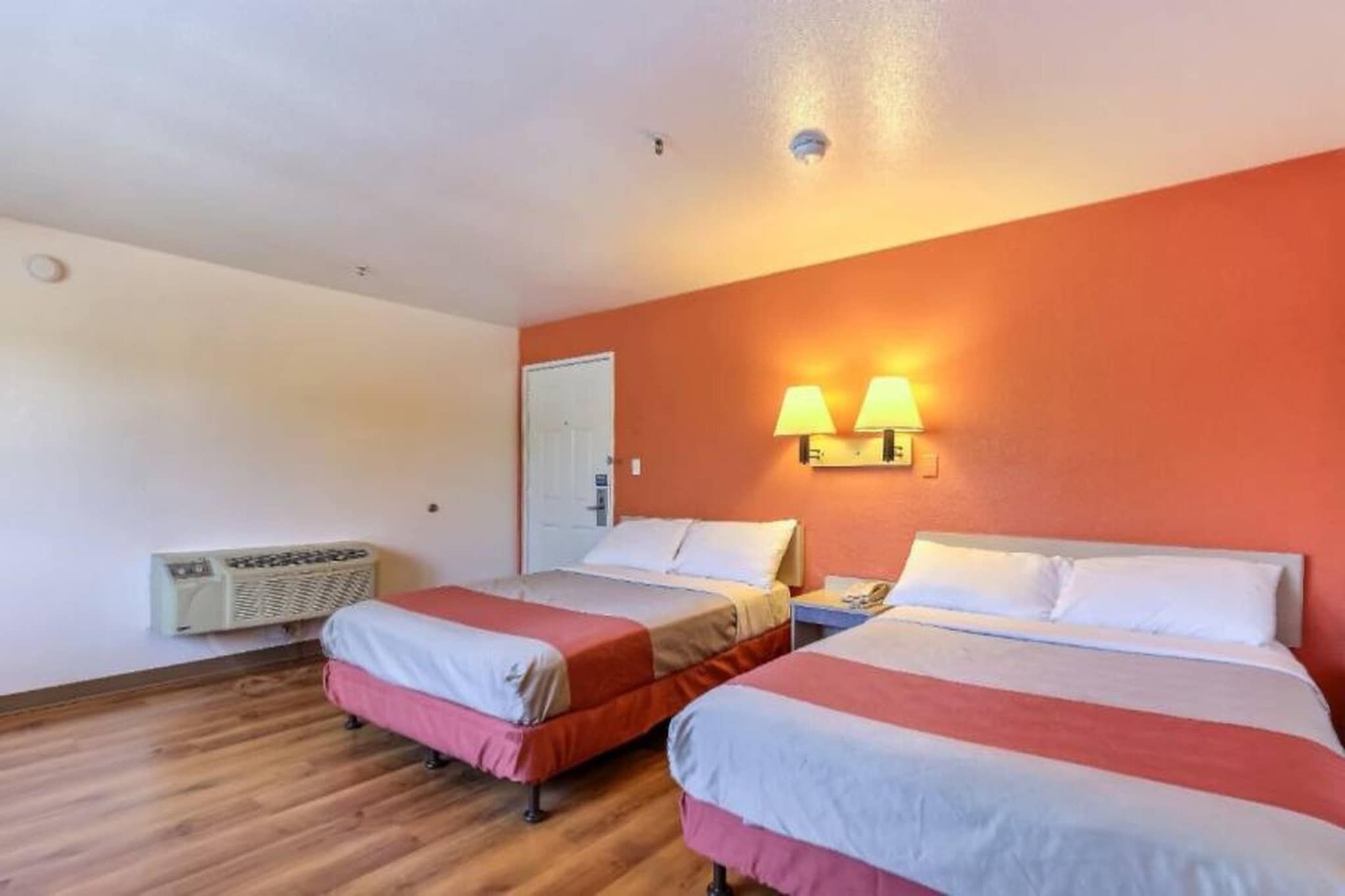 A hotel room with two beds, a heater, and two wall-mounted lamps.