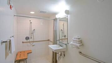 A bathroom with a shower, sink, and handrails.