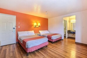 Une chambre d’hôtel avec deux lits, un plancher en bois, une porte blanche et une salle de bain visible à travers une porte ouverte.