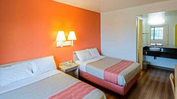 A hotel room with two beds, a nightstand, a bathroom with a sink, and a mirror.