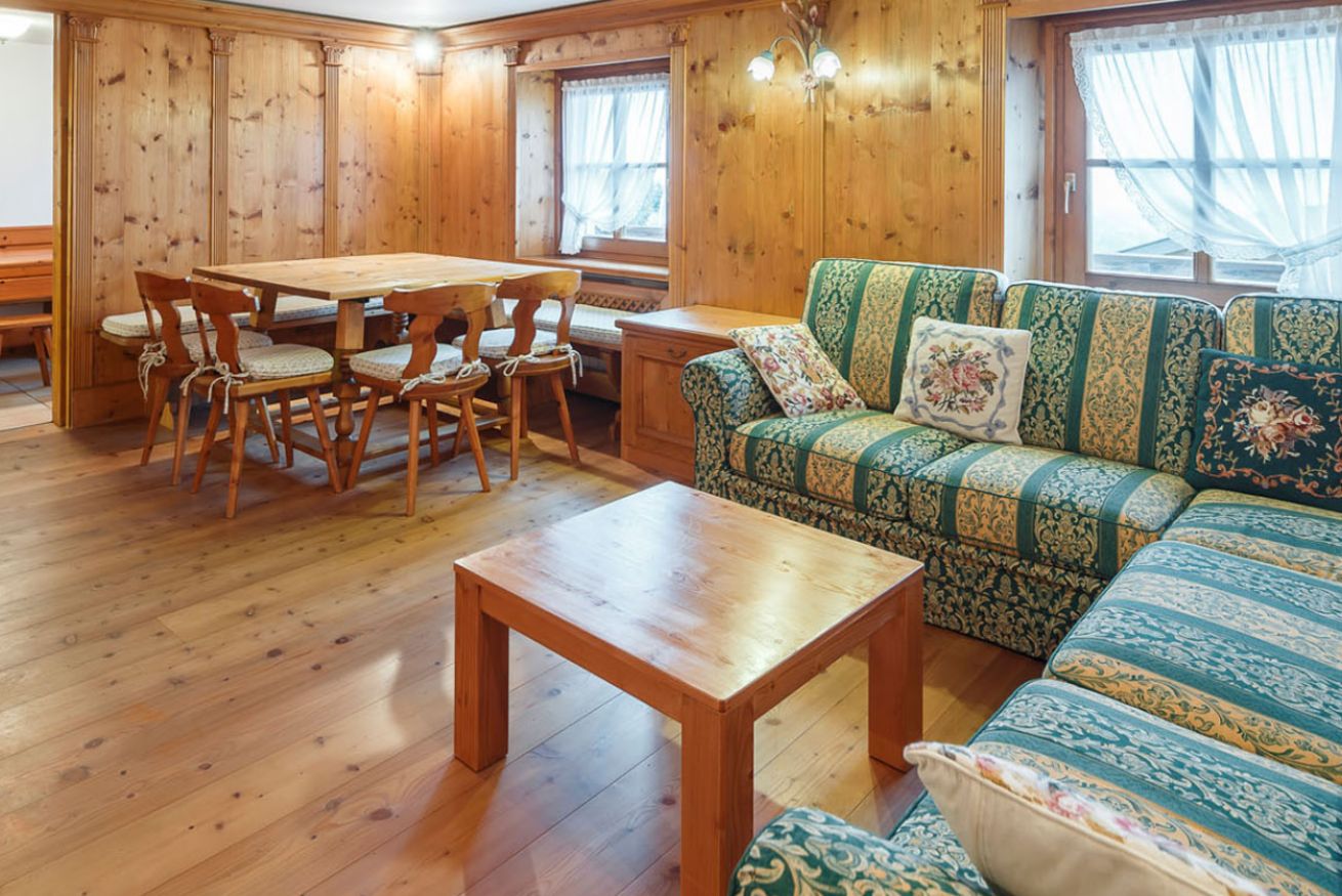 Una habitación con paneles de madera, una mesa de comedor, sillas y un sofá con cojines estampados.