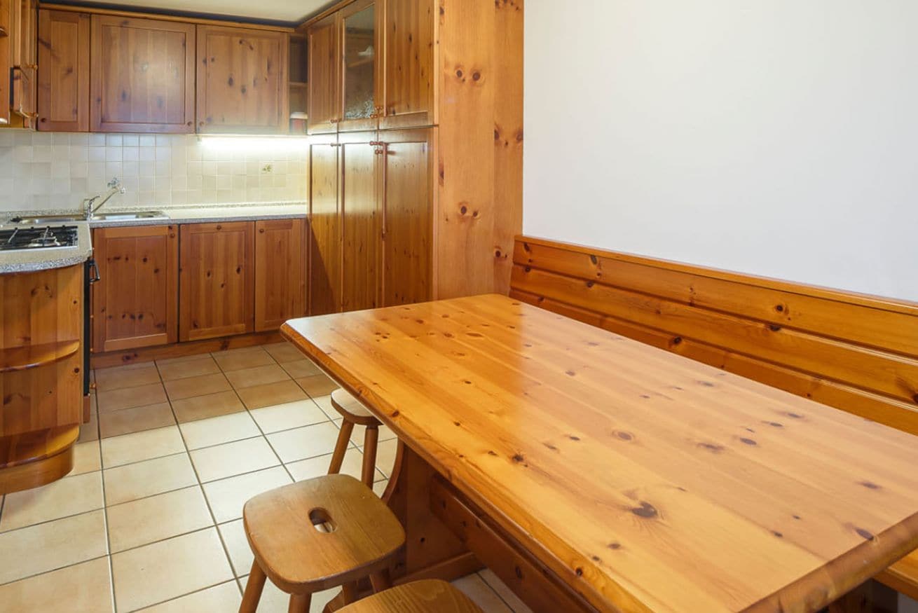 A kitchen with wooden cabinets, a wooden table, and two stools.
