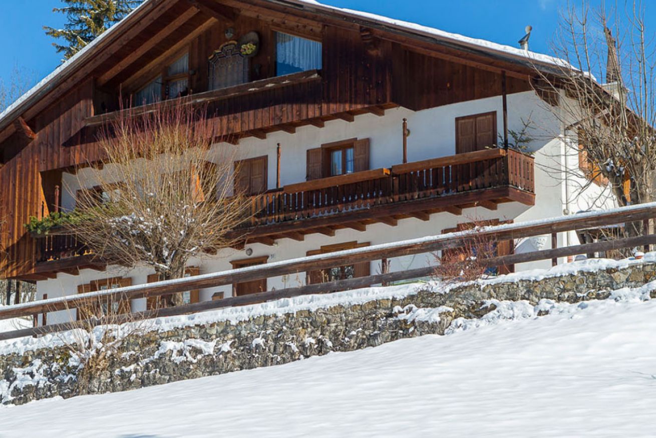 Una cabaña de madera con base de piedra, varios balcones y un paisaje cubierto de nieve.