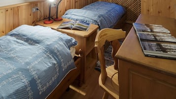 A room with two wooden beds, a desk with a lamp, and a chair.
