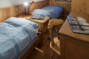 A room with two wooden beds, a desk with a lamp, and a chair.