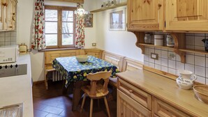Eine Küche mit Holzausstattung, einem Tisch mit Blumenmuster bedeckter Tischdecke, einem Stuhl und einem Fenster mit Vorhängen.