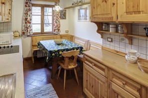 Una cucina con mobili in legno, un tavolo con tovaglia floreale, una sedia e una finestra con tende.
