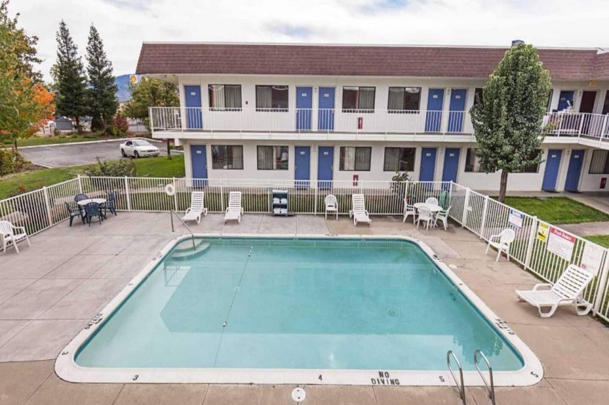 Um motel com piscina, área de estar externa e um prédio de dois andares com portas azuis.