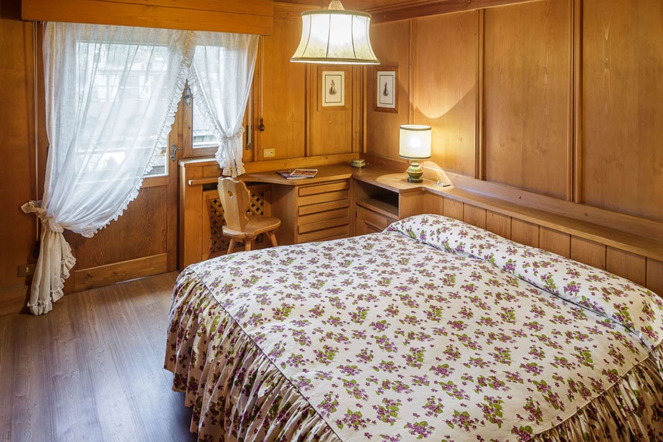 A bedroom with a bed, a desk, a chair, and a window with curtains.