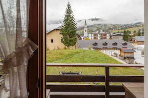A view from a window overlooking a town with a church, a large tree, and a grassy area. - Apartment for 4 in the Heart of Cortina with Parking (Cortina d'Ampezzo)