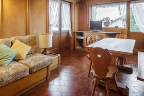 Una habitación acogedora con un sofá de madera, una mesa de comedor con sillas, un televisor y una ventana con cortinas.