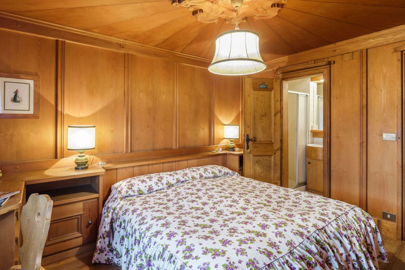 A wooden-paneled room with a bed, two bedside tables, a desk, and a door.