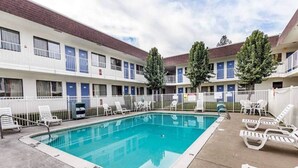 Un hotel con piscina, mobiliario exterior y zona vallada.