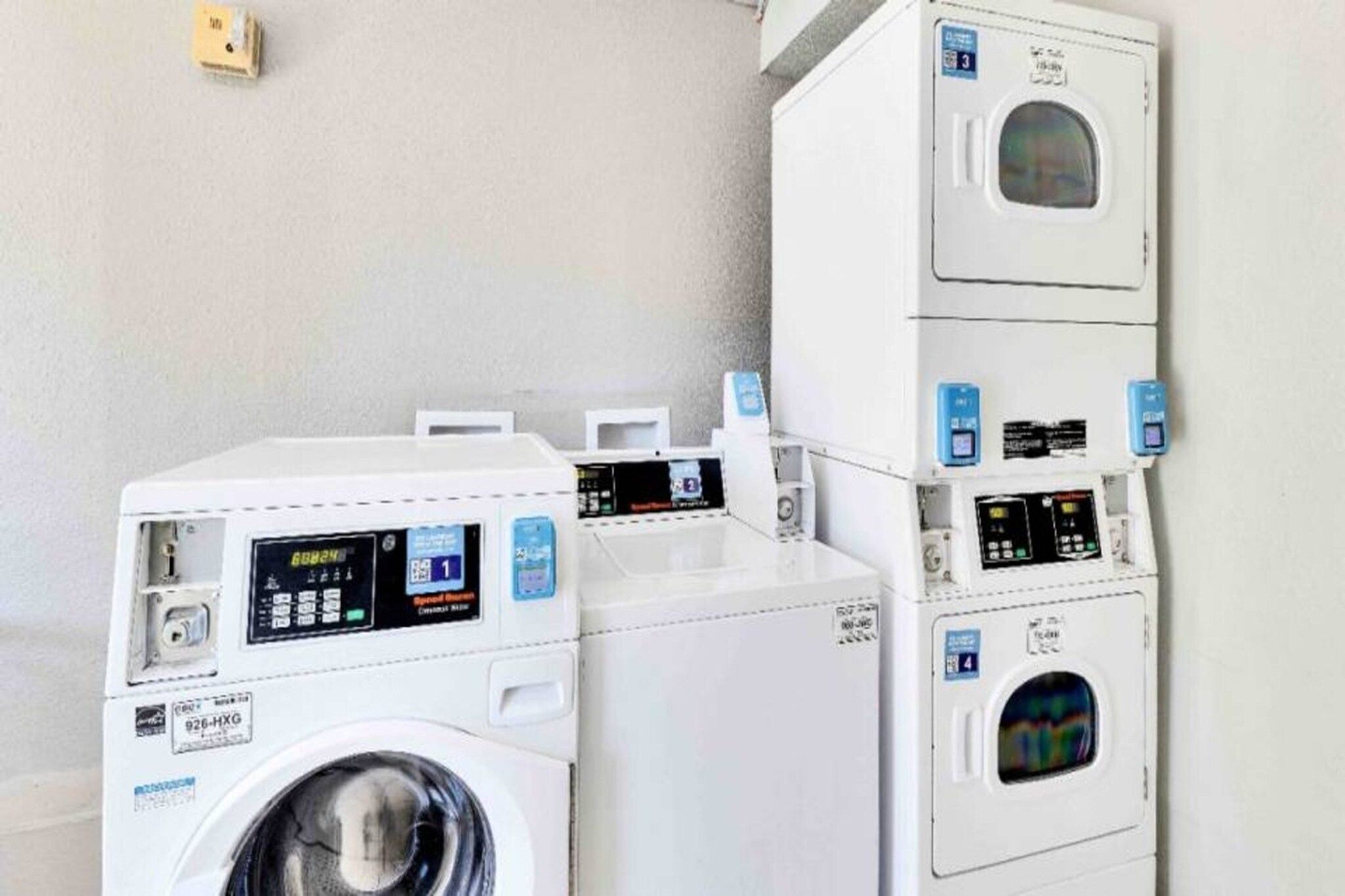 A laundry facility with multiple washing machines and dryers, each with a control panel and a digital display.