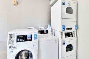 A laundry facility with multiple washing machines and dryers, each with a control panel and a digital display.