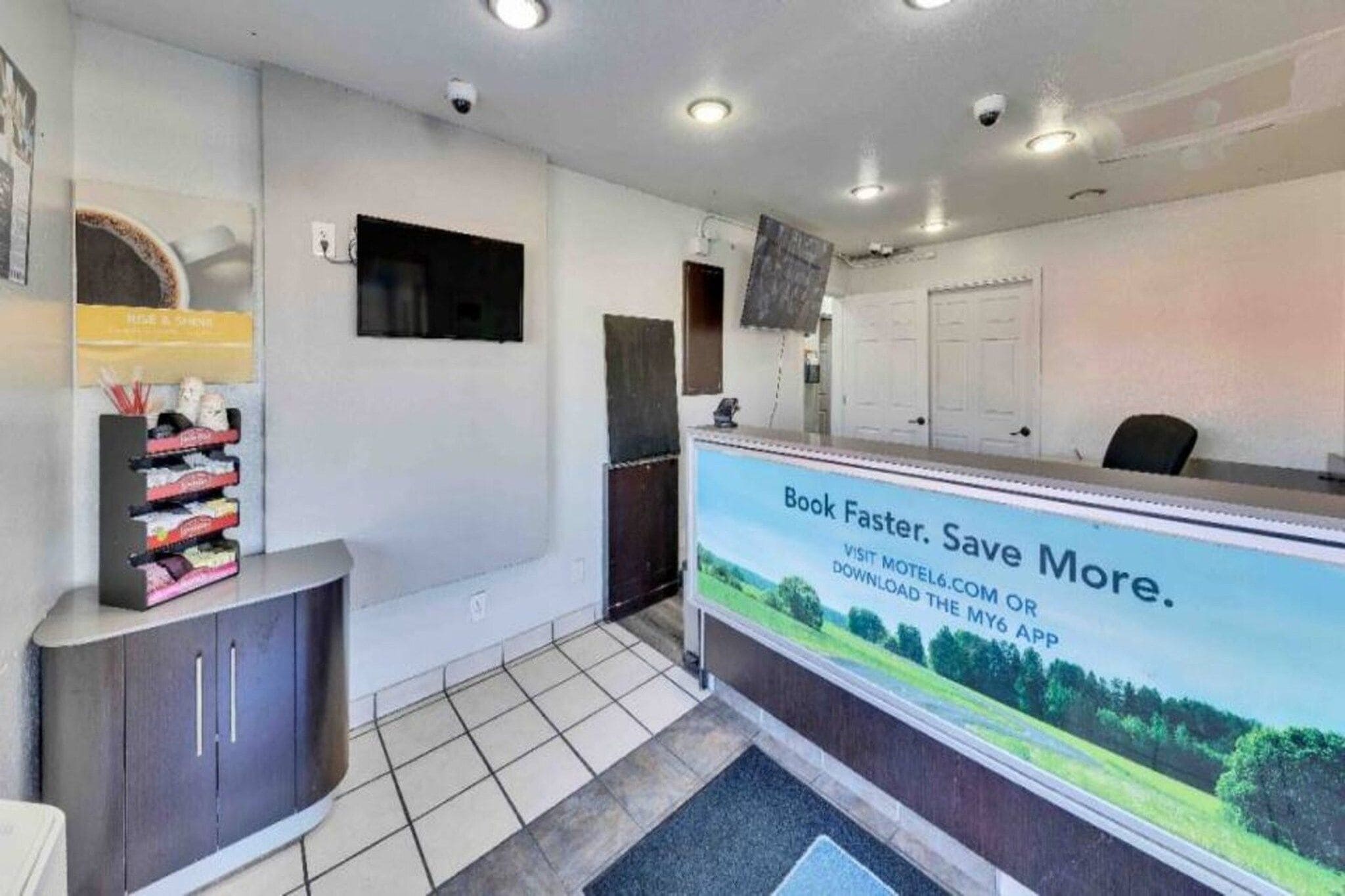 A reception desk with a sign promoting a booking app. There is a tiled floor, a dark-colored cabinet, and a wall-mounted television.