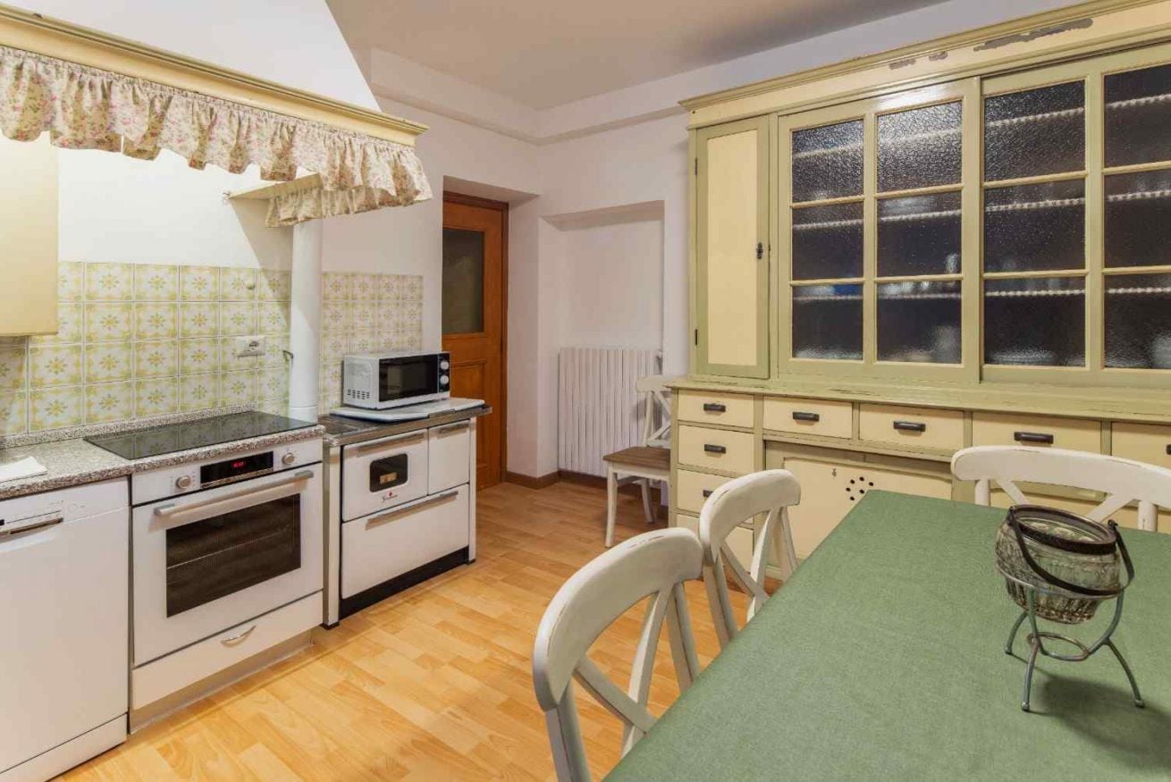 A kitchen with a microwave, oven, and cabinets. There is a dining table with chairs.
