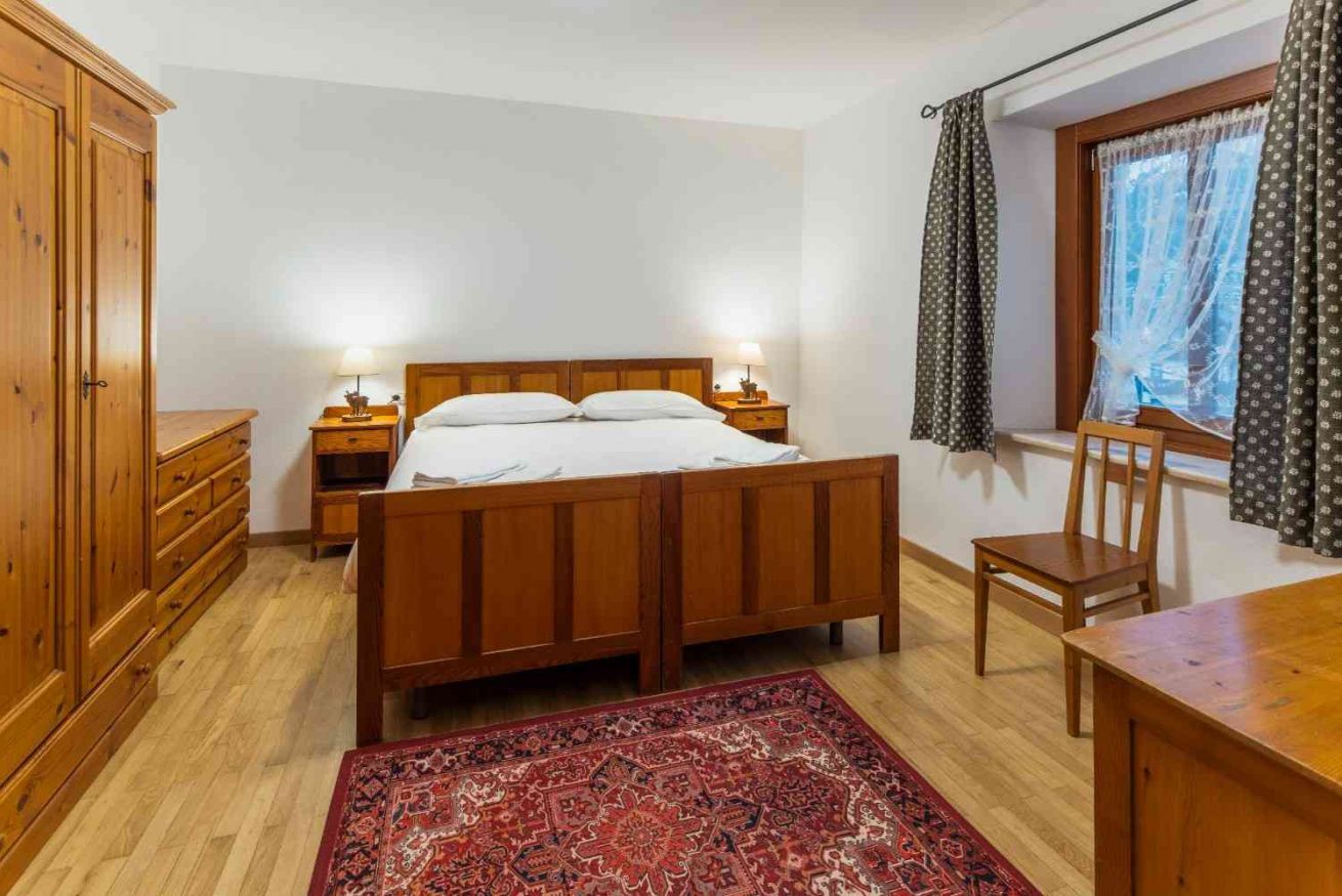 Una camera da letto con un letto in legno, comodini, una sedia, un armadio e una finestra con tende.