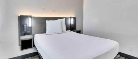 A modern hotel room with a large bed, two bedside tables, and wall-mounted lighting.