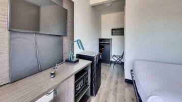 A modern hotel room with a flat-screen TV, a desk with a lamp, a microwave, and a dining area with a chair.