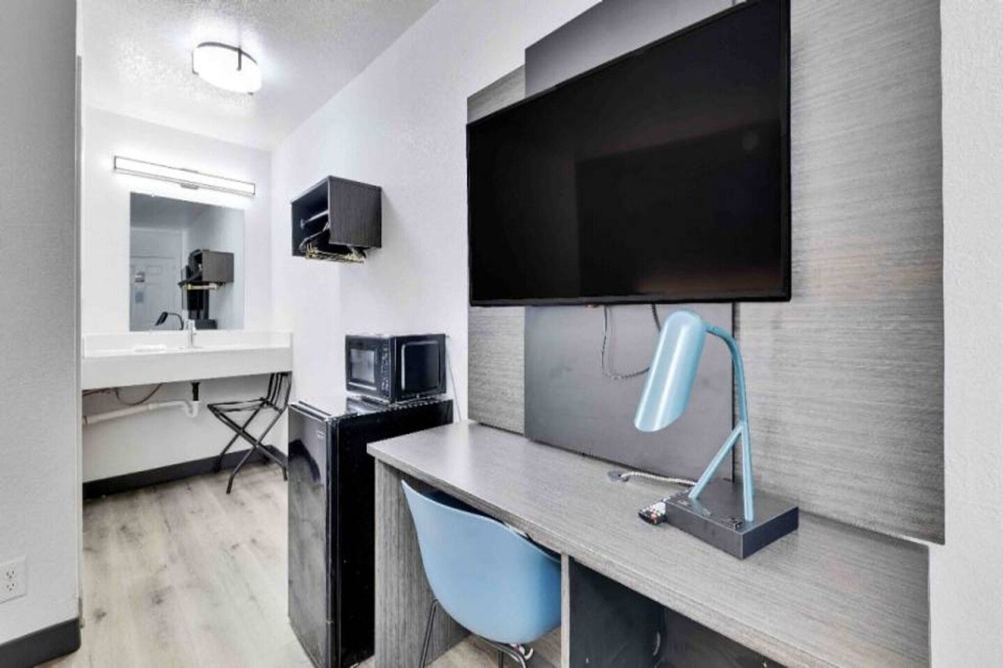 Habitación de hotel moderna con televisor de pantalla plana en la pared, un escritorio con silla y una pequeña área de cocina.