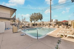 A swimming pool with lounge chairs and a tree in the background. - ADA 1 Full Bed | Tub (Austin)