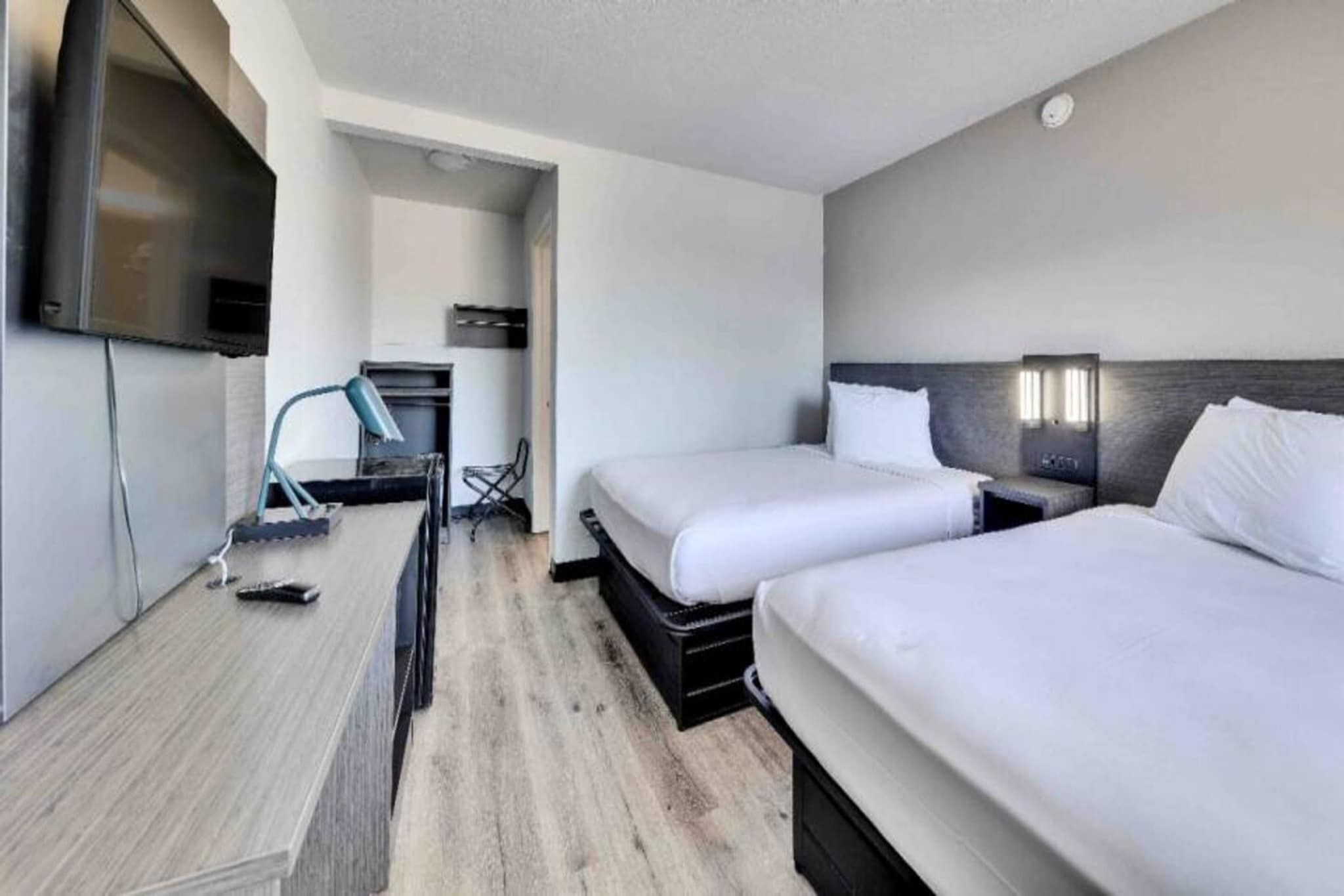A hotel room with two beds, a desk, a chair, a TV, and a small kitchenette.