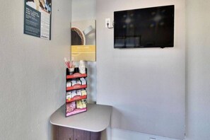 Een hoek van een kamer met een klein tafeltje waarop een stapel kleurrijke spullen staat, een lichtschakelaar aan de muur en een raam met uitzicht.