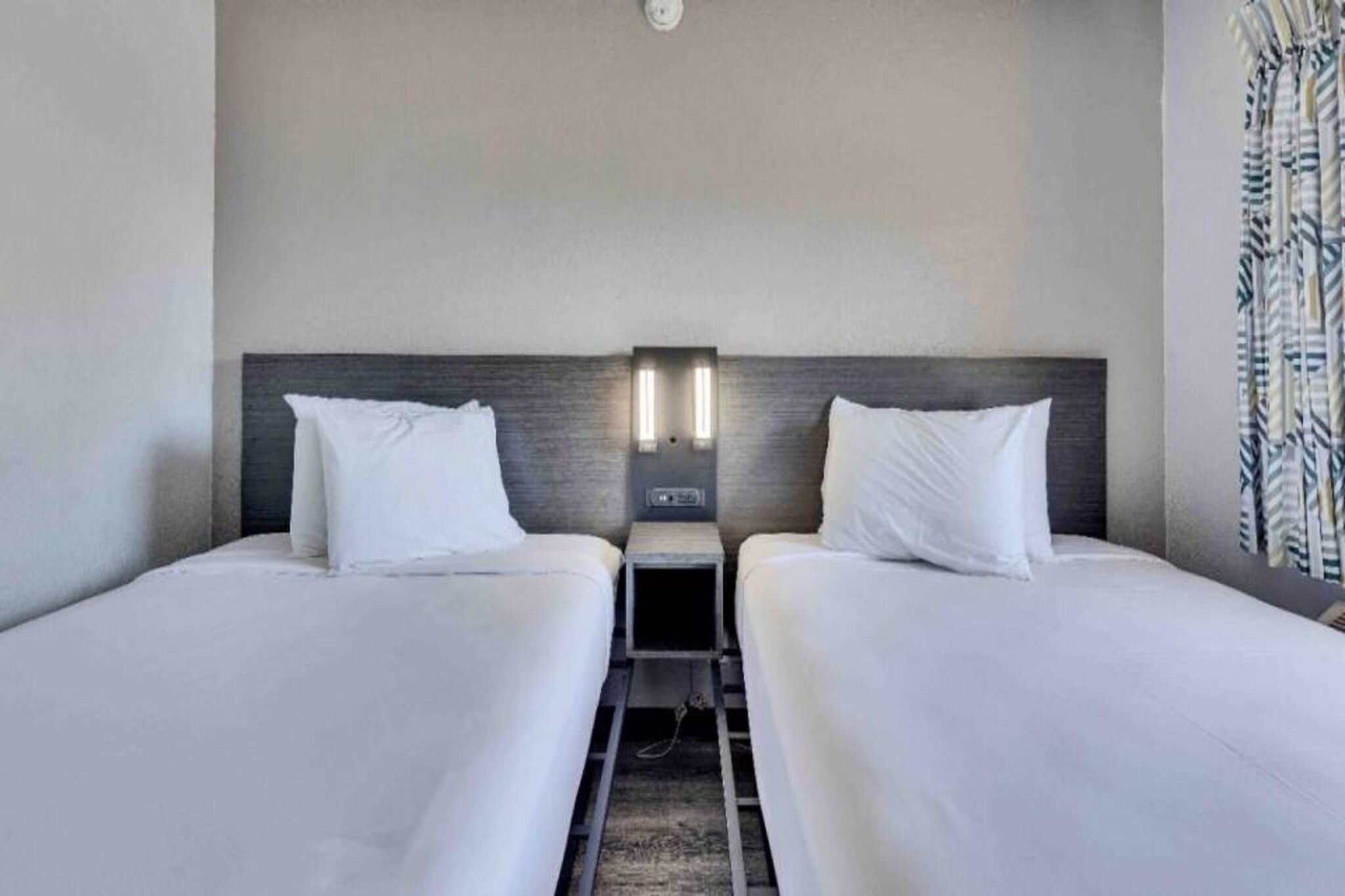 A hotel room with two beds, a nightstand, and a wall-mounted light fixture.