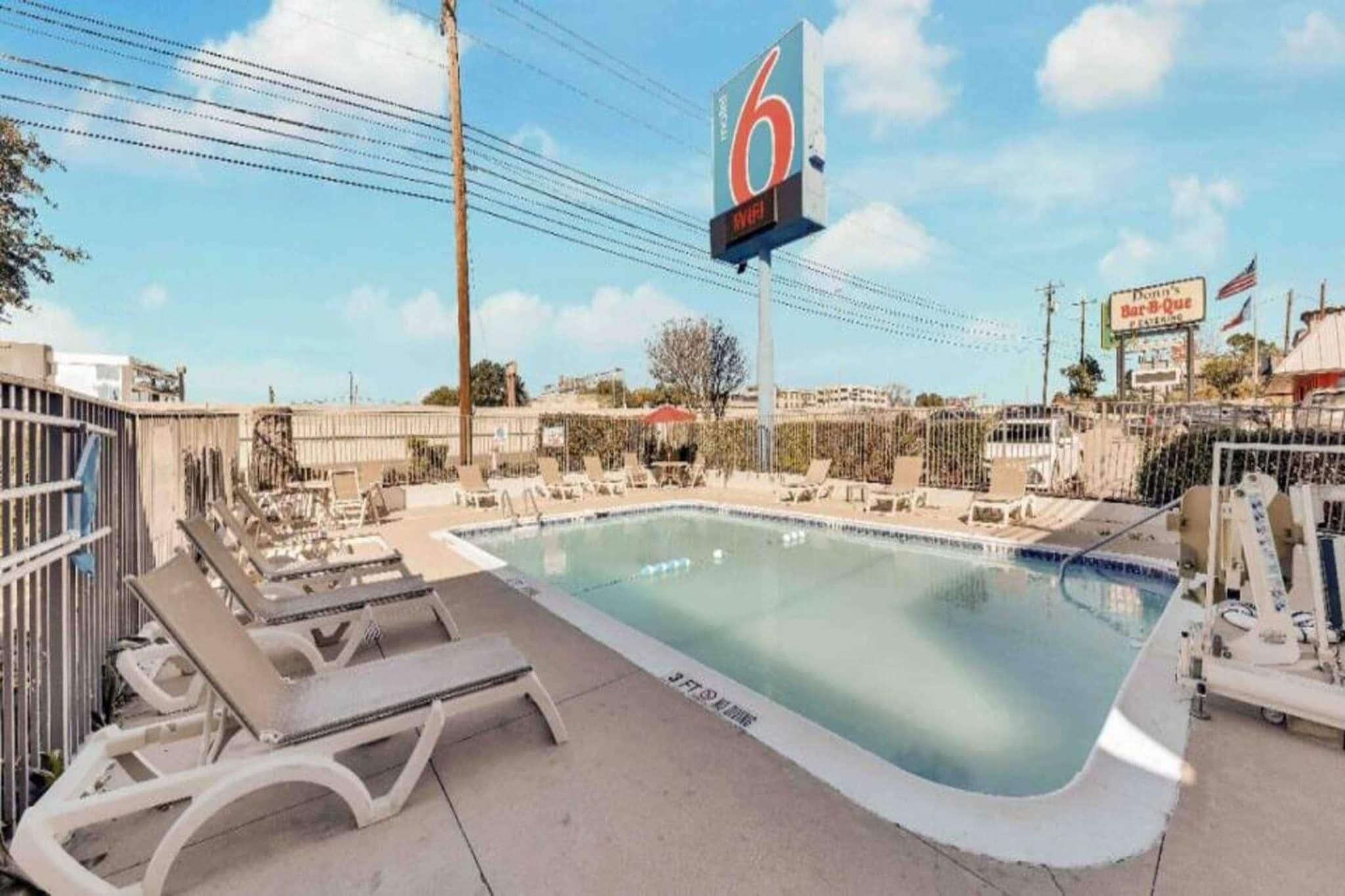 A swimming pool with lounge chairs, a large sign with the number 6, and a fenced area.