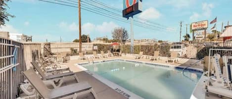 A swimming pool with lounge chairs, a large sign with the number 6, and a fenced area.