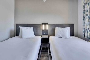 Habitació d'hotel amb dos llits, una tauleta de nit i una làmpada de paret.