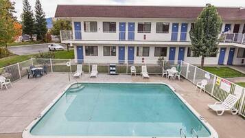 A motel with a swimming pool, outdoor seating, and a two-story building with blue doors.