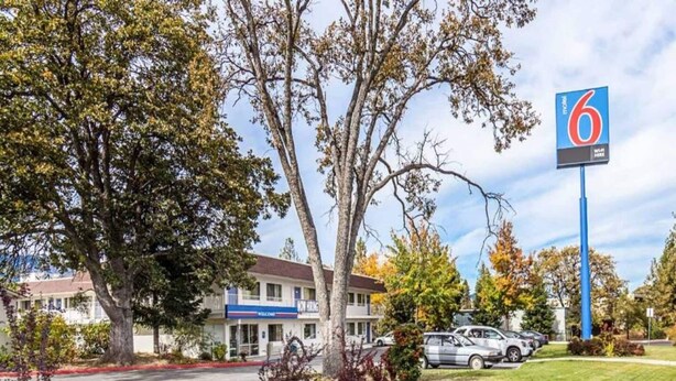 Un motel con un letrero que dice '6', un estacionamiento y un edificio con un cartel de 'Nuevo empleado'.