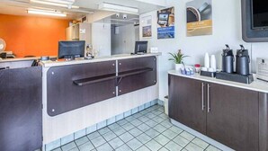 Zona de recepción con mostrador, computadoras, máquina de café y una planta en maceta.