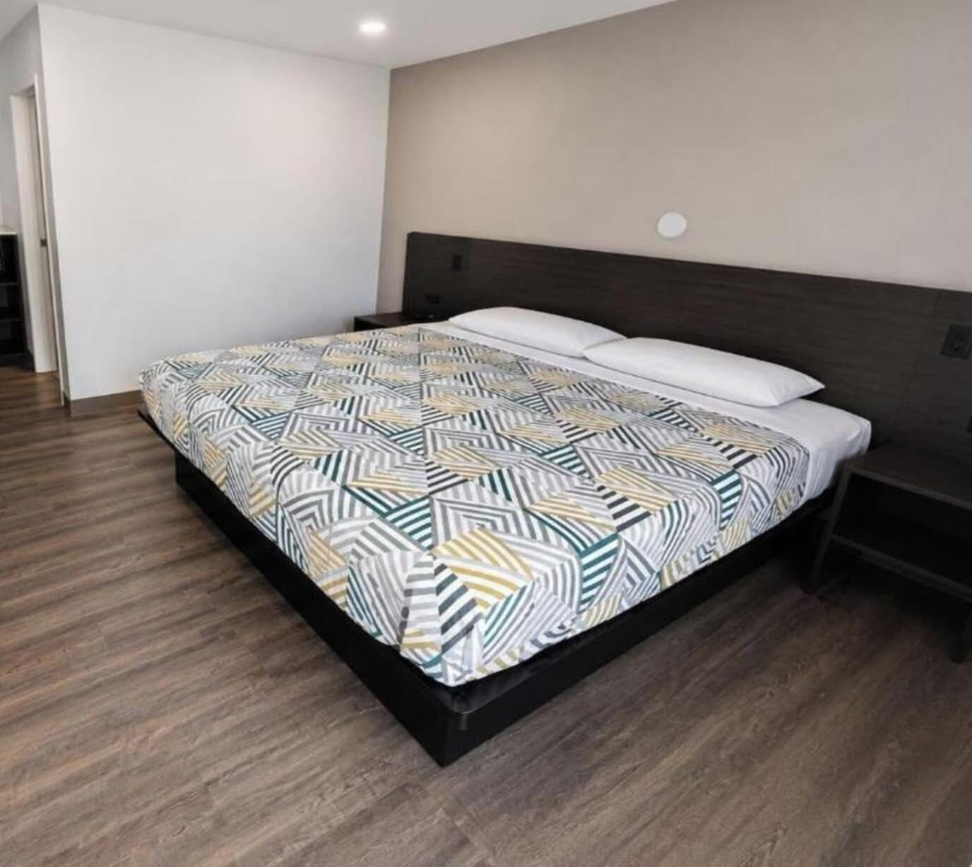 Quarto moderno com uma cama grande, cabeceira escura e piso de madeira.