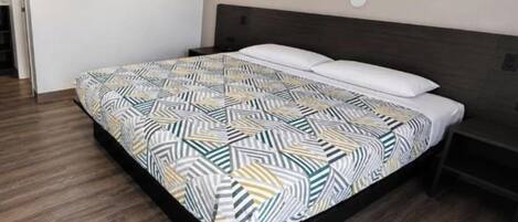 A modern bedroom with a large bed, a dark headboard, and a wooden floor.