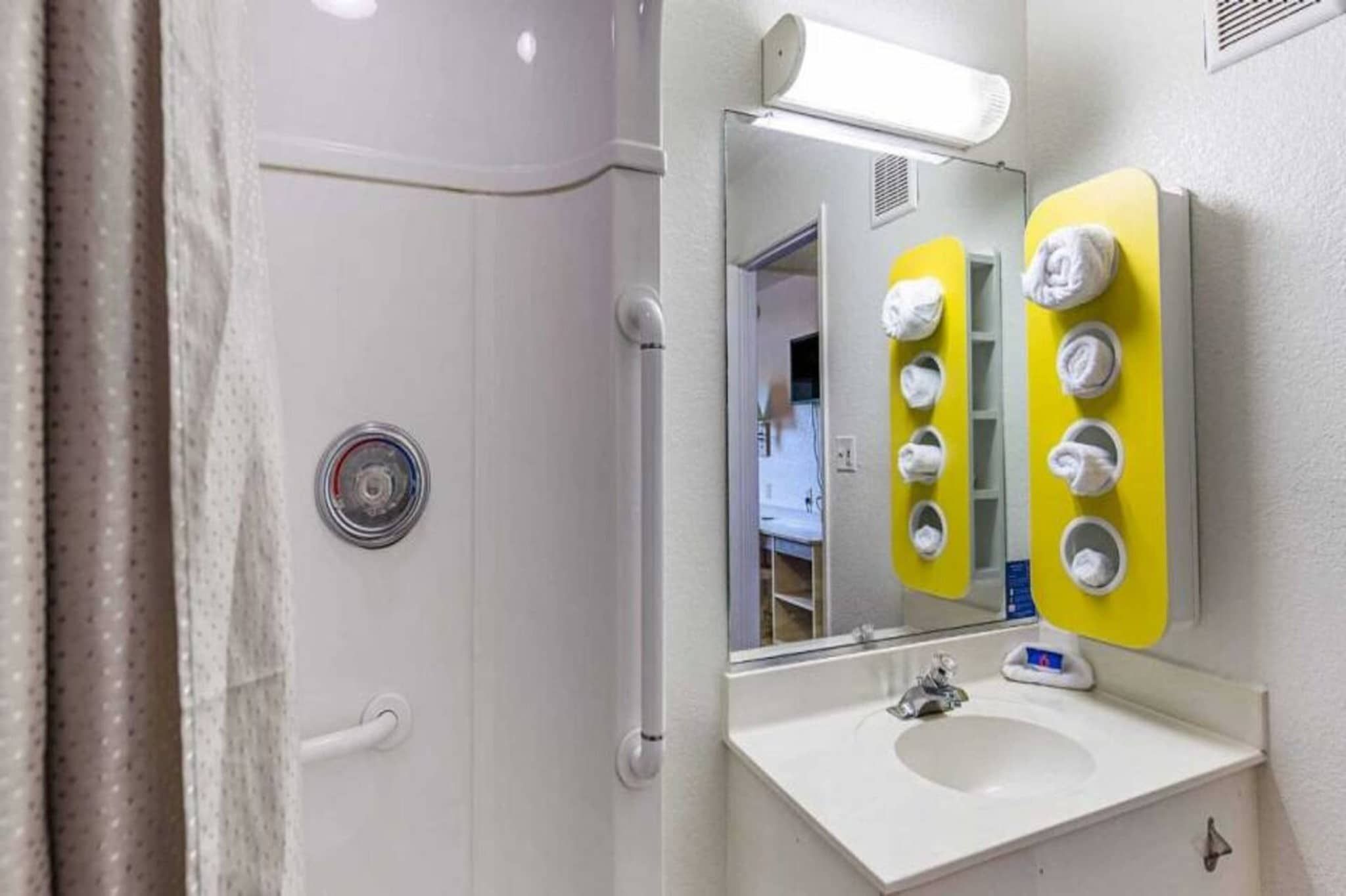 Un baño con ducha, lavamanos y espejo con ganchos para toallas.