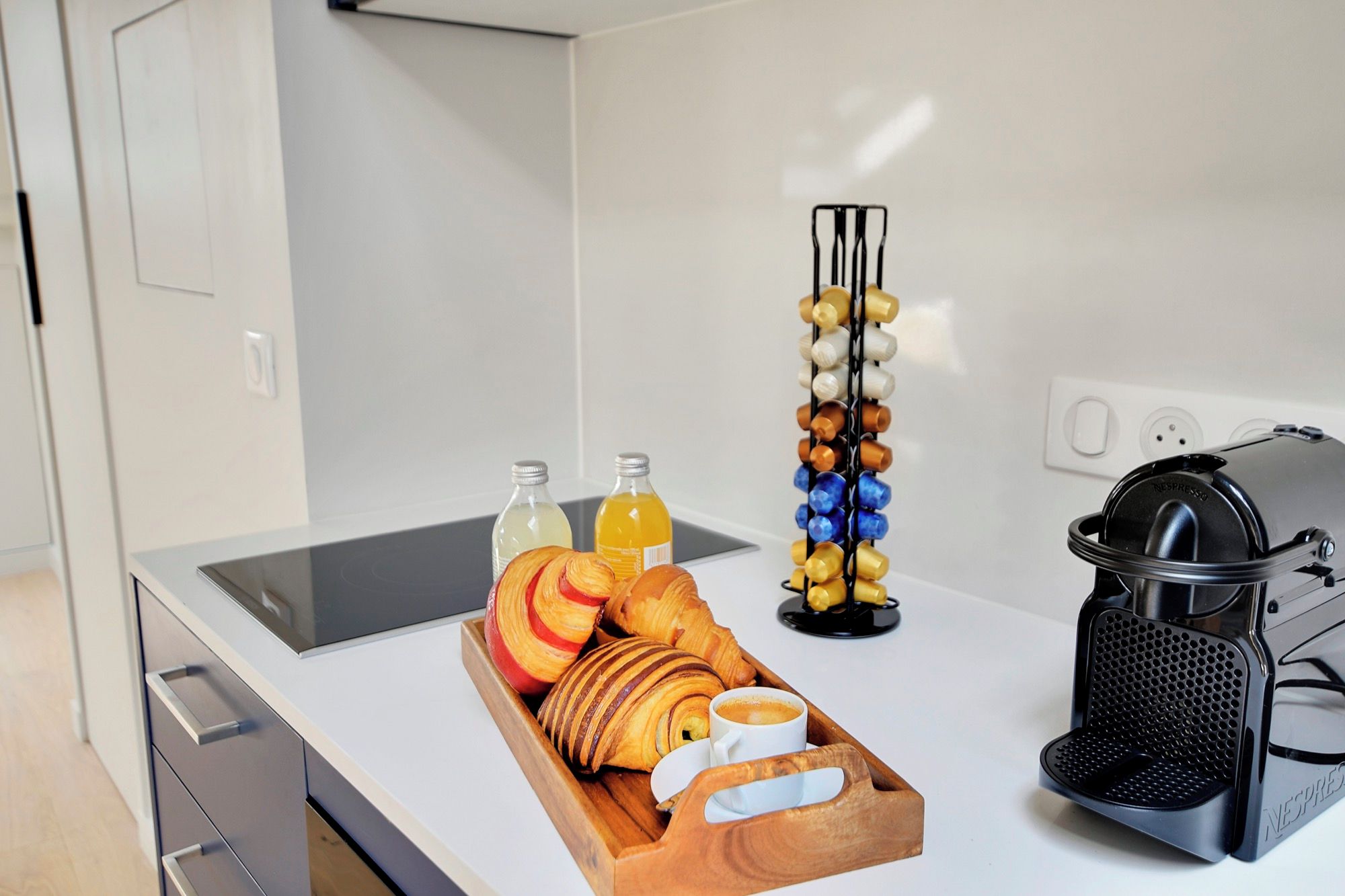 A kitchenette with a coffee maker, a bottle of orange juice, a bottle of water, a tray of croissants, and a coffee cup.