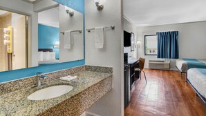 A hotel room with a granite countertop sink, a flat-screen TV, a bed with a blue and white bedspread, and a wooden floor. - 1 King Bed | Non-Smoking (Norcross)