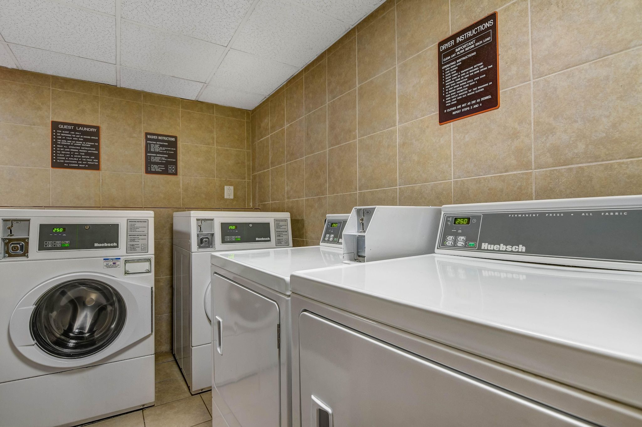A laundry facility with multiple machines, including a front-loading washer and a top-loading dryer, and clear instructions on the wall.