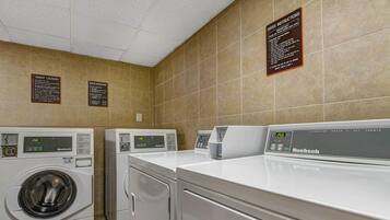 A laundry facility with multiple machines, including a front-loading washer and a top-loading dryer, and clear instructions on the wall.