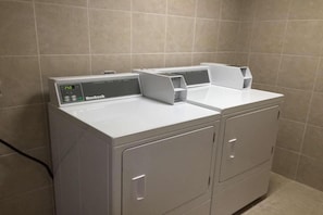 Eine Frontlader Waschmaschine und Trocknerkombination in Weiß mit digitaler Anzeige, platziert in einem Badezimmer mit Fliesenwänden.