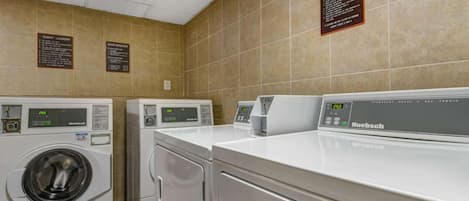 A laundry facility with multiple machines, including a front-loading washer and a top-loading dryer, with instructions and labels on the wall.