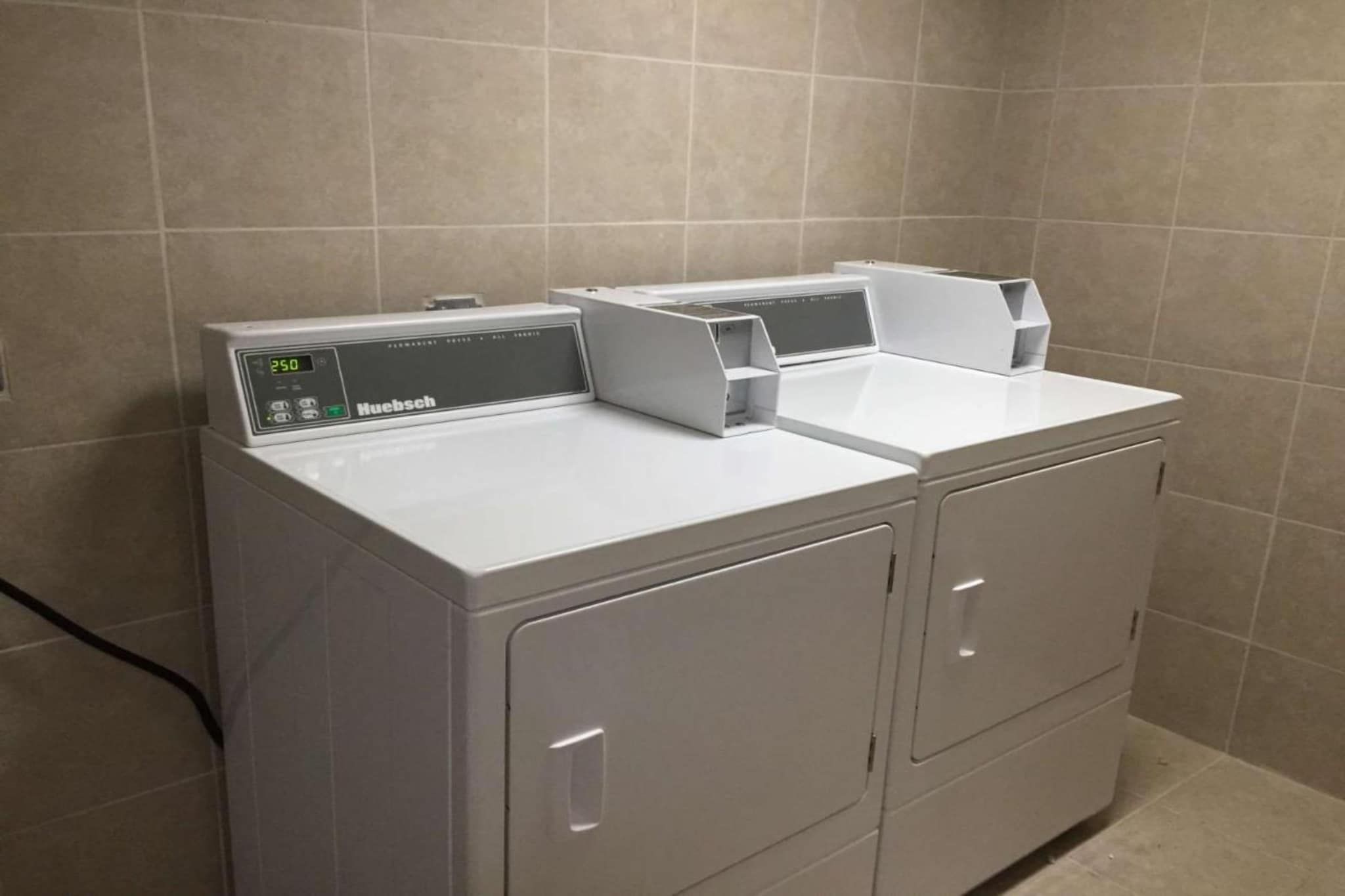 Lavadora y secadora apilables de color blanco con carga frontal y pantalla digital, ubicadas en un baño con paredes de azulejos.