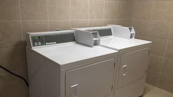 Lavadora y secadora apilables de color blanco con carga frontal y pantalla digital, ubicadas en un baño con paredes de azulejos.