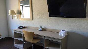 Habitación de hotel con escritorio, silla, lámpara, teléfono y televisor de pantalla plana montado en la pared.