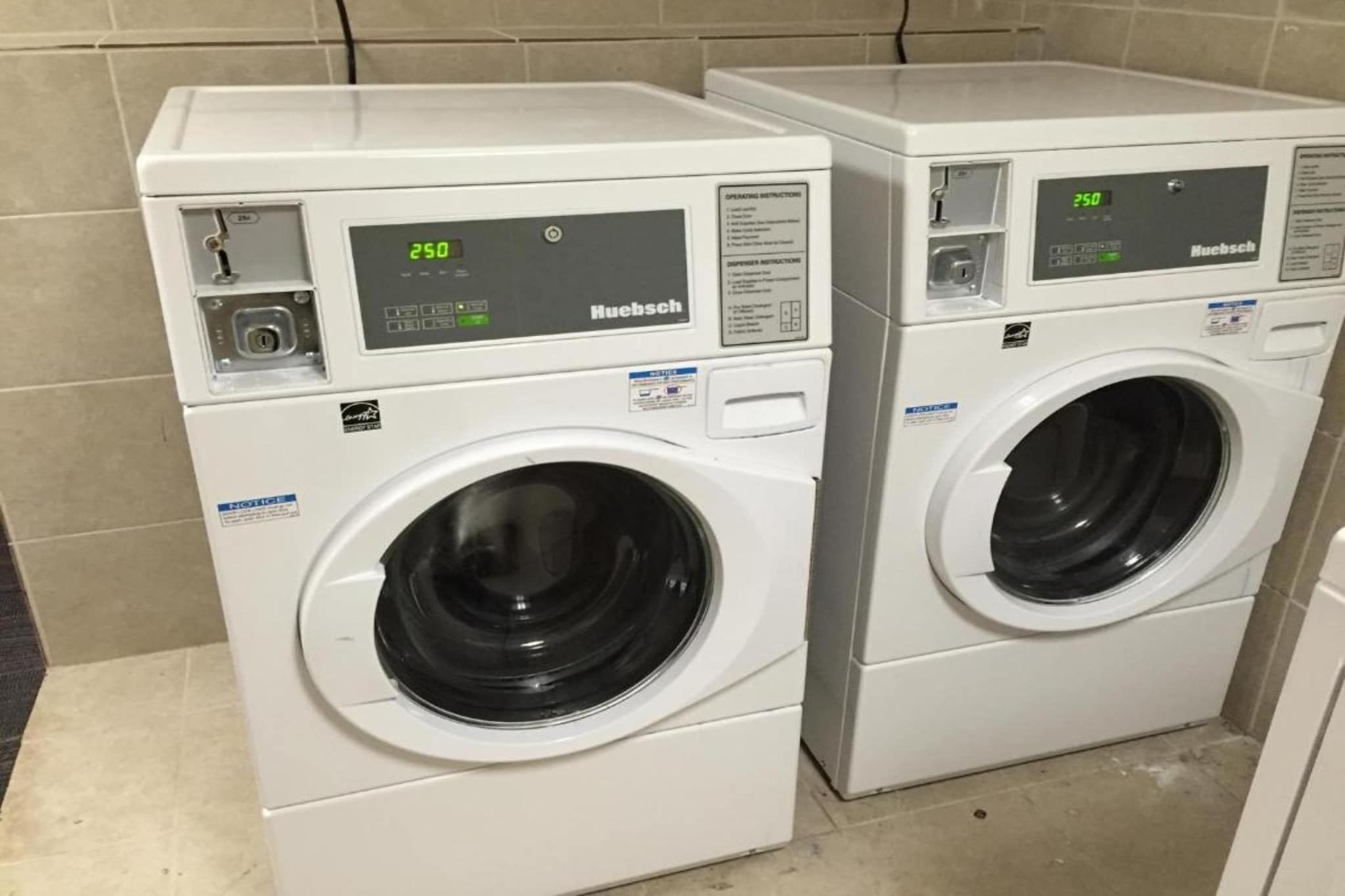 Two white front-loading washing machines with digital displays, placed in a tiled area.