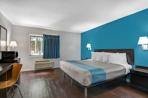 A hotel room with a bed, a desk, a chair, a window with curtains, and a wall-mounted lamp. - 1 King Bed|Mobility|Tub|Smk (Norcross)